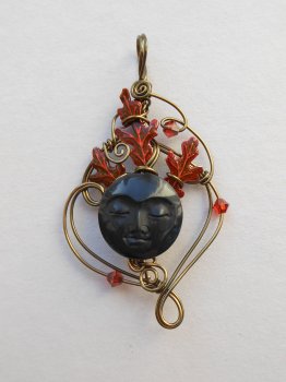 Antique brass wire pendant, red oak leaves behind a round black carved face Antique brass wire pendant, red oak leaves behind a round black carved face